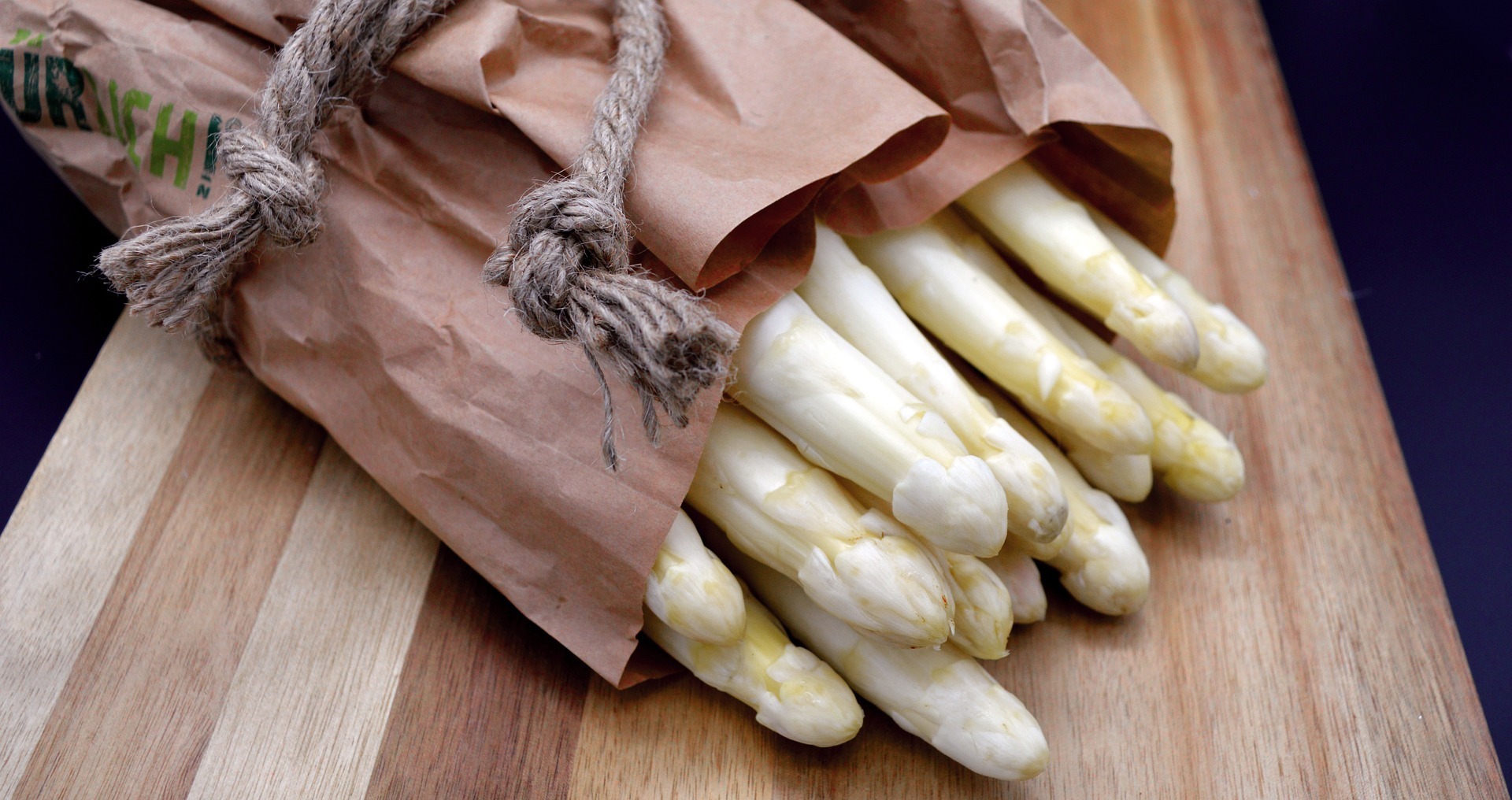 Weißer Spargel in Papier auf einem Holzbrett
